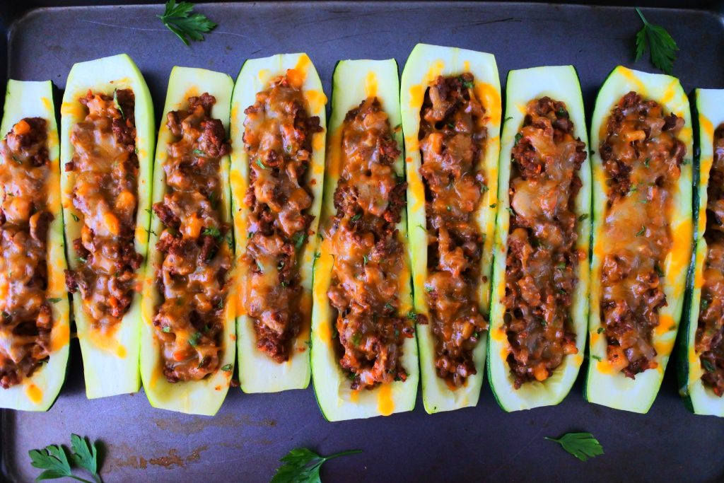 An overhead image of baked zucchini boats next to each other on a tray with leaves of fresh parsley around it