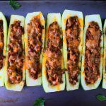 An overhead image of baked zucchini boats next to each other on a tray with leaves of fresh parsley around it