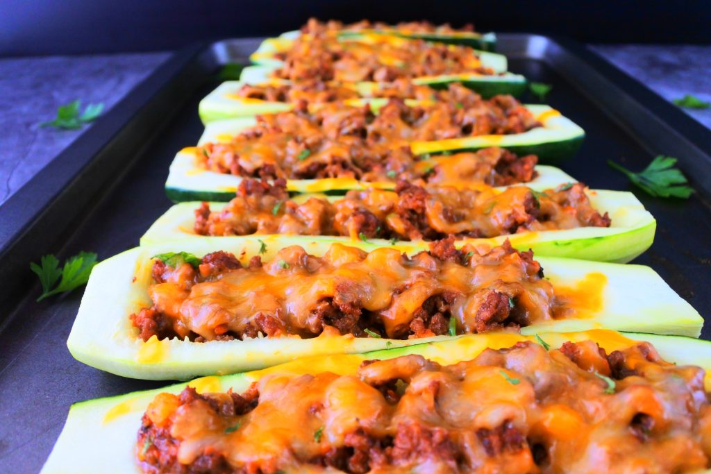 A head on angled image of baked zucchini boats next to each other on a tray with leaves of fresh parsley around it