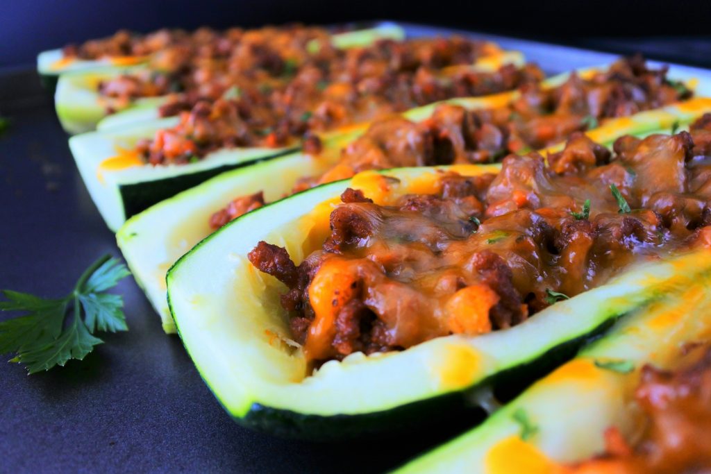 An angled image of baked zucchini boats next to each other on a tray with leaves of fresh parsley around it
