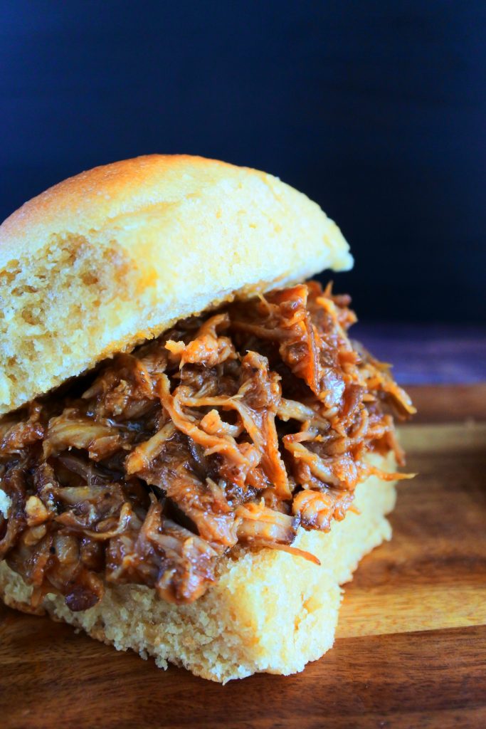 Head on image of a bbq pulled pork slider on a homemade roll set on a wooden board.