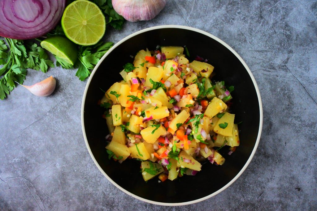 An overhead image of a bowl of pineapple salsa with fresh herbs in the top left corner