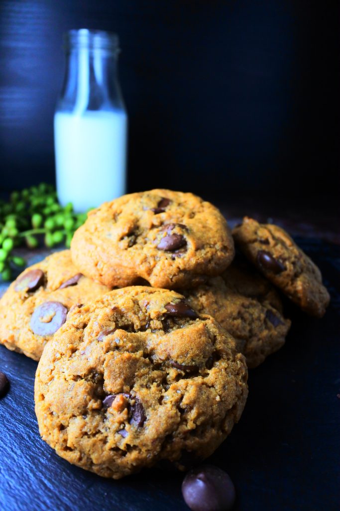 A pile of classic chocolate chip cookies with a bottle of milk in the background