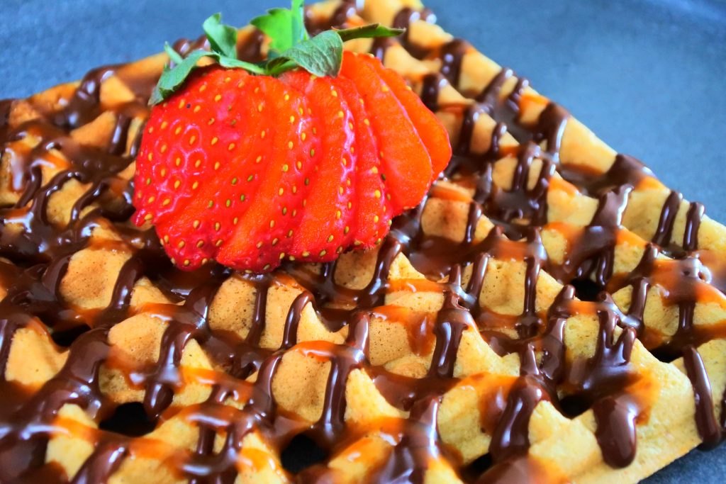 A close up image of a waffle with a chocolate and salted caramel drizzle with a sliced strawberry on top.
