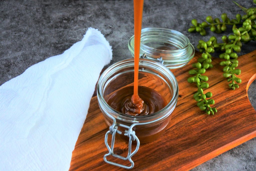 An angled image of a small jar with salted caramel being poured into it.