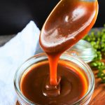 An angled image of a jar of salted caramel sauce with a spoon of caramel drizzling down back into the jar
