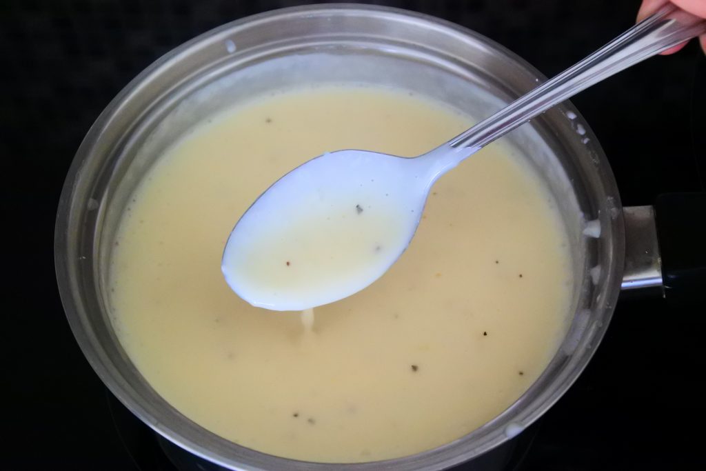 An angled image image of a spoon lifted out of a pot of Alfredo sauce