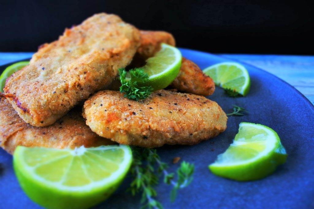 A head on image of a plate of crispy fried fish fillets garnished with herbs and lime wedges