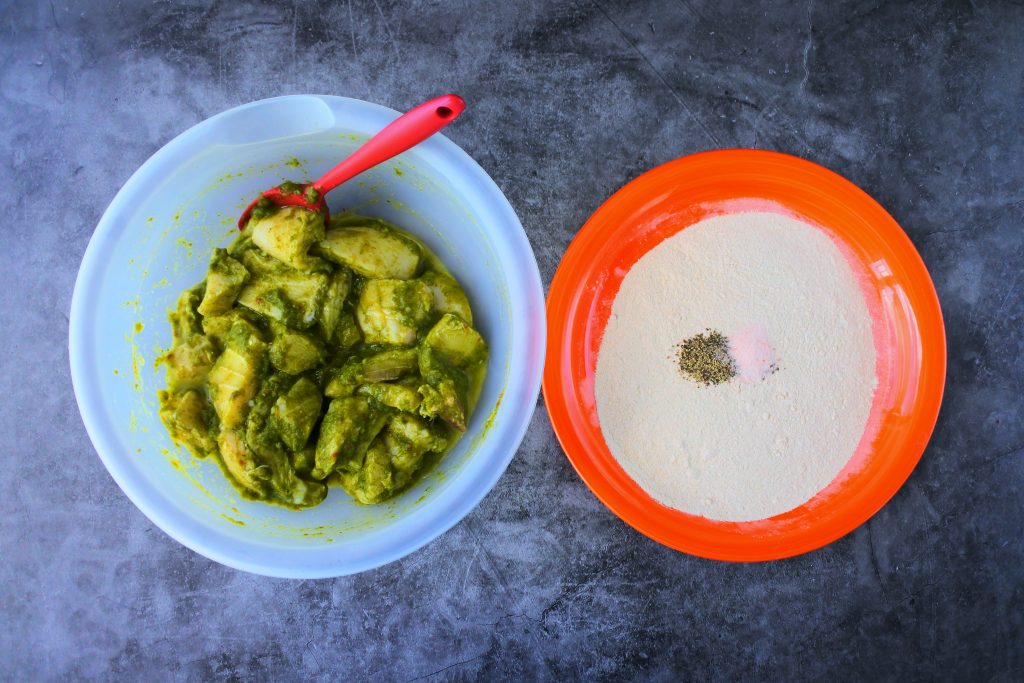 An overhead image of a bowl of seasoned fish fillets and a plate of flour with salt and pepper added to it