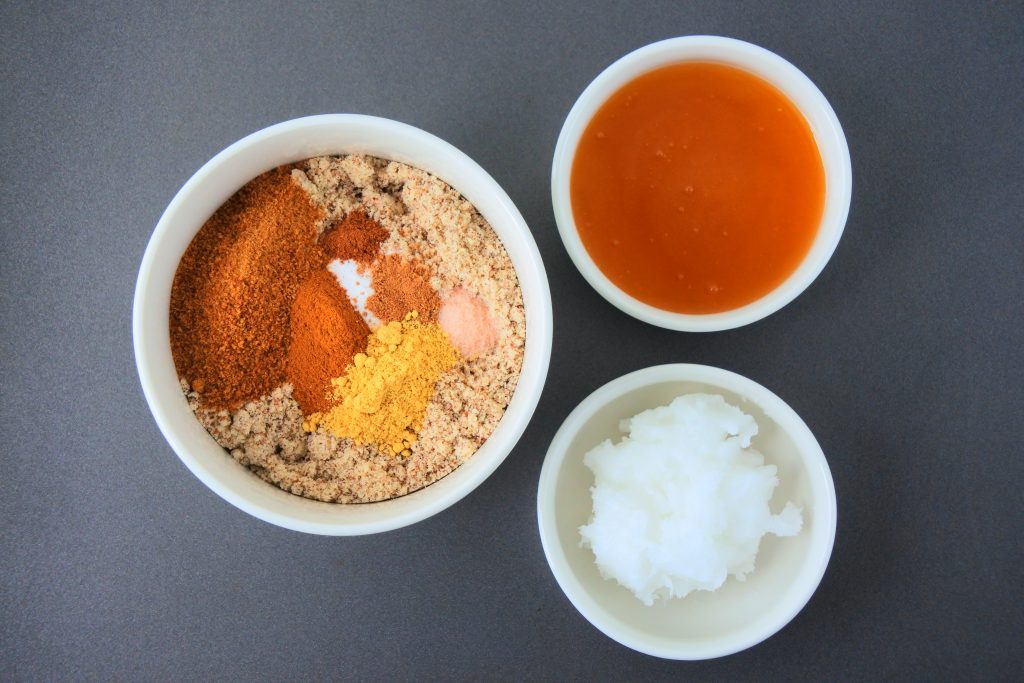 An overhead image of a bowl of dry ingredients for gingerbread cookie dough, next to a small bowl of honey and another dish of coconut oil