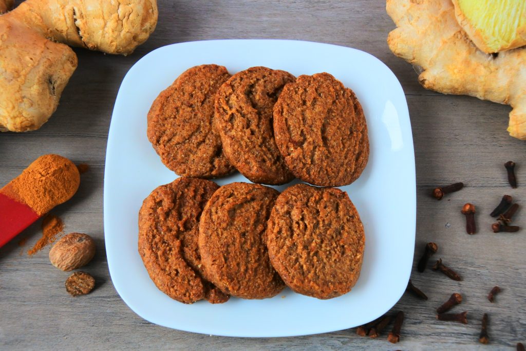 An overhead image of a plate of six gingerbread cookies surrounded by spices
