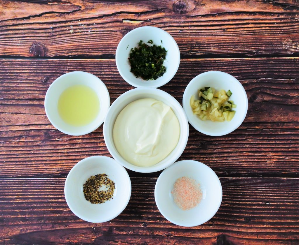 An overhead image of dishes of ingredients for a tartar sauce including Greek Yogurt, homemade pickles, salt, pepper, lemon juice and dill