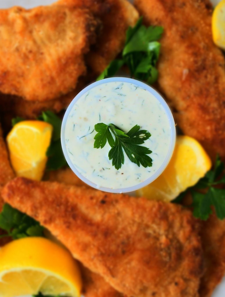 A close up image of a dish of tartar sauce surrounded by lightly fried fish fillets