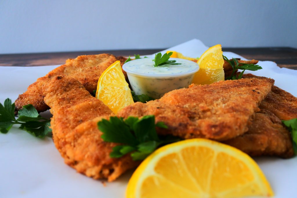 A head on image of lightly fried fish fillets served with a tartar sauce, lemon wedges and parsley