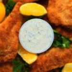A close up image of a dish of tartar sauce surrounded by lightly fried fish fillets