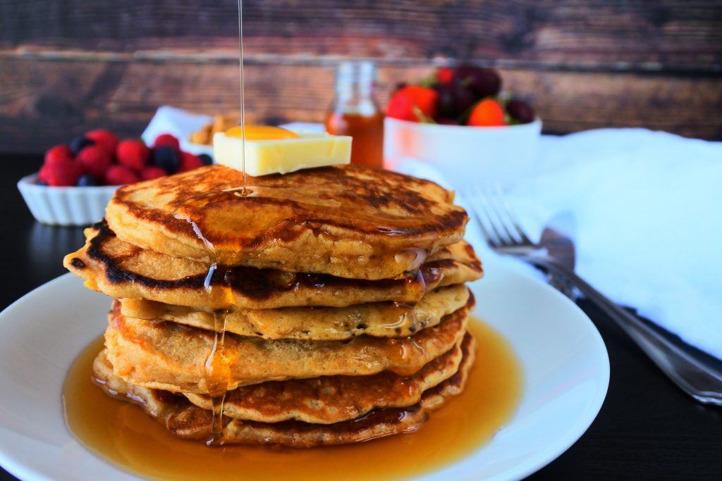 A stack of whole wheat buttermilk pancakes topped with butter and syrup being poured over it