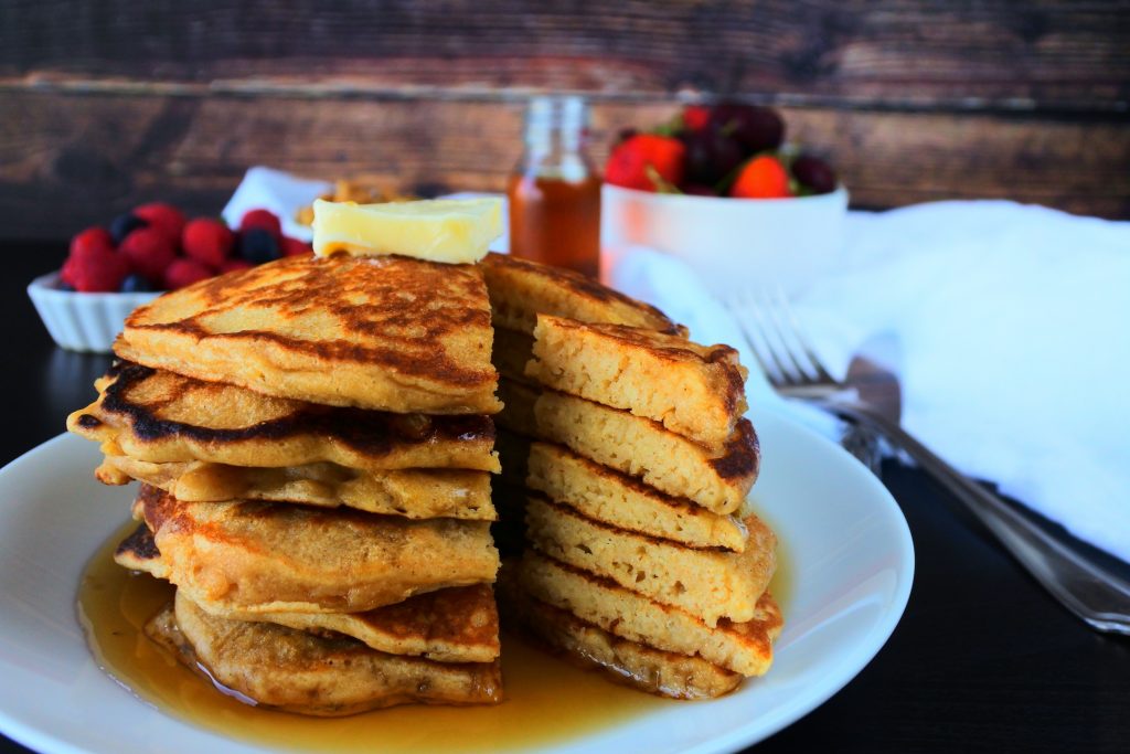 A head on image of a stack of sliced pancakes topped with butter and syrup