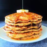 A stack of whole wheat buttermilk pancakes topped with butter and syrup being poured over it