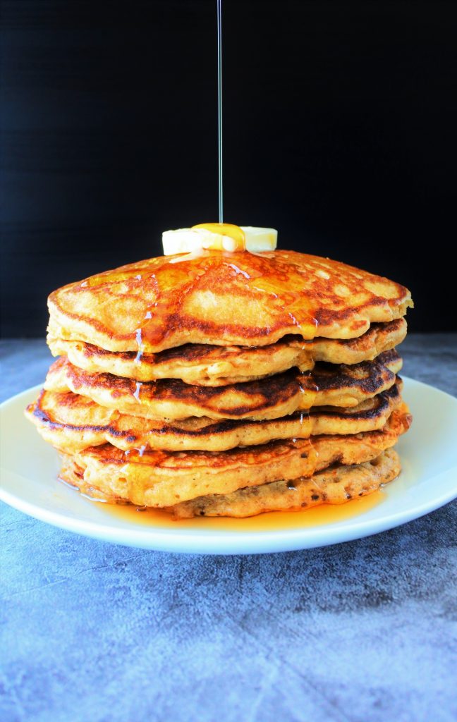 A stack of whole wheat buttermilk pancakes topped with butter and syrup being poured over it