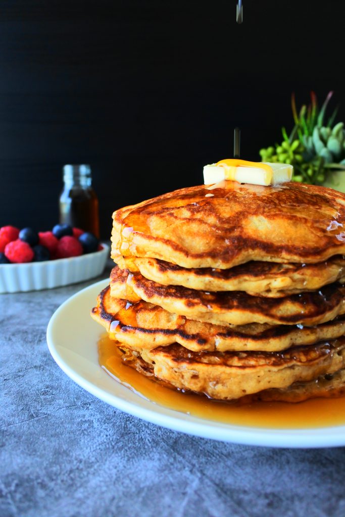 A stack of whole wheat buttermilk pancakes topped with butter and syrup being poured over it