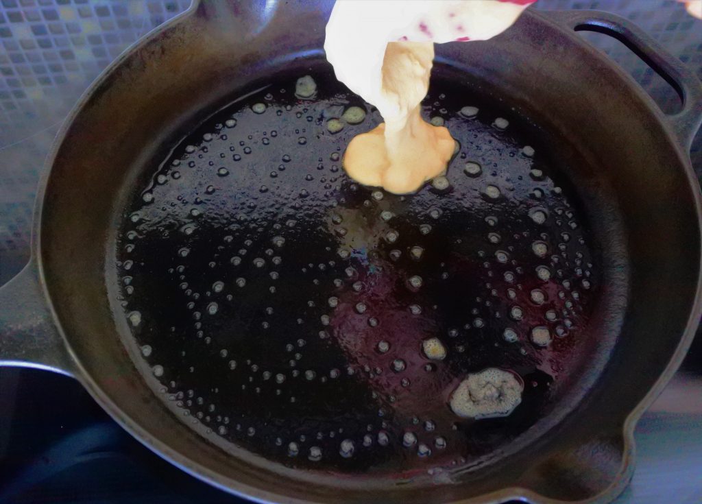 An angled image of of pancake batter being poured into a hot and greased skillet