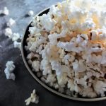 An vertical angled overhead bowl of popcorn with scattered kernels and coarse grain salt on the work surface