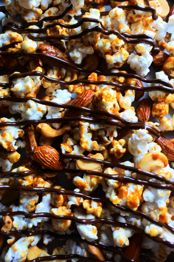 An overhead image of caramel popcorn with nuts and chocolate stripes