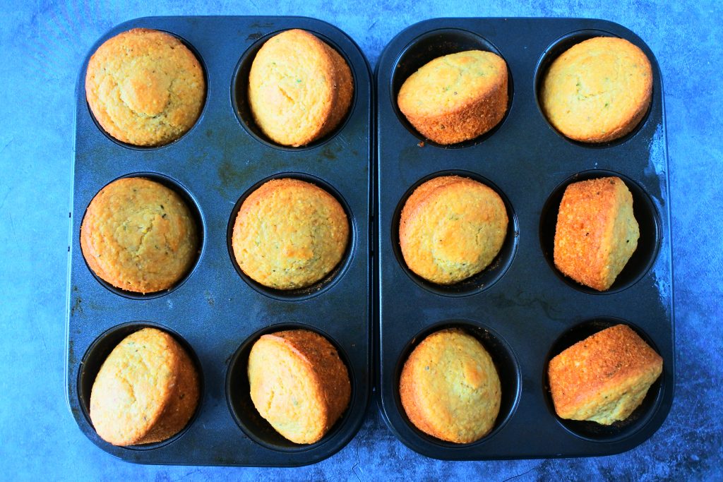 An overhead image of a dozen cornbread muffins angled and cooling in a muffin pan