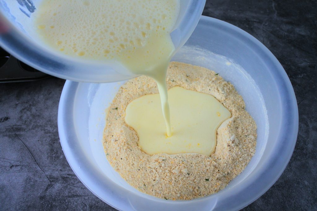 An overhead image of wet ingredients being poured into the dry ingredients for cornbread muffins