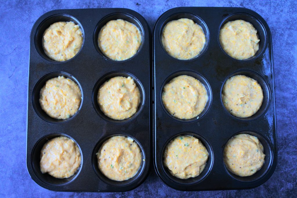 An overhead image of cornmeal muffin batter divided evenly into a dozen muffin pan molds
