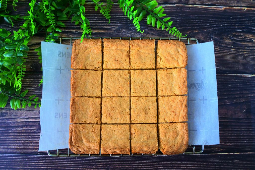 An overhead image of a tray of boterkoek on a cooling rack cut into squares