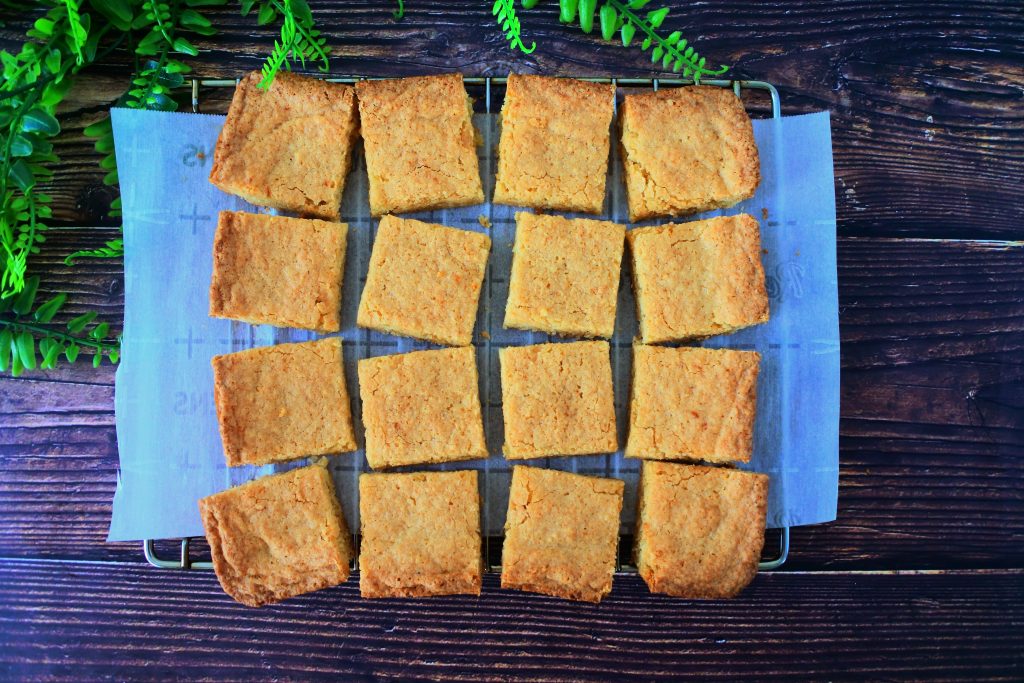 An overhead image of a tray of boterkoek on a cooling rack cut into squares