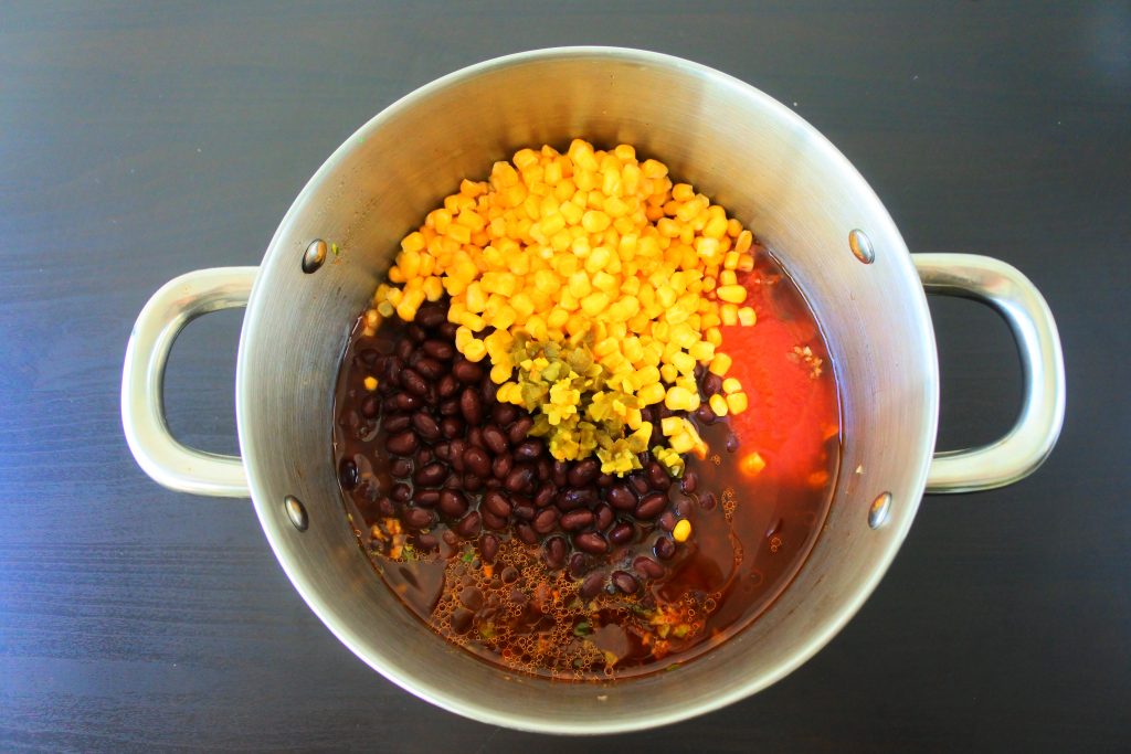 An overhead image of a pot with various ingredients for Kitrusys chili being added in