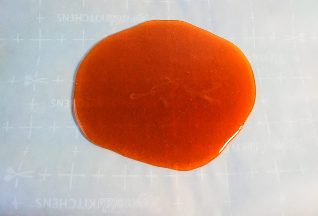 An angled image of ginger honey candy syrup after being poured onto parchment and left to cool