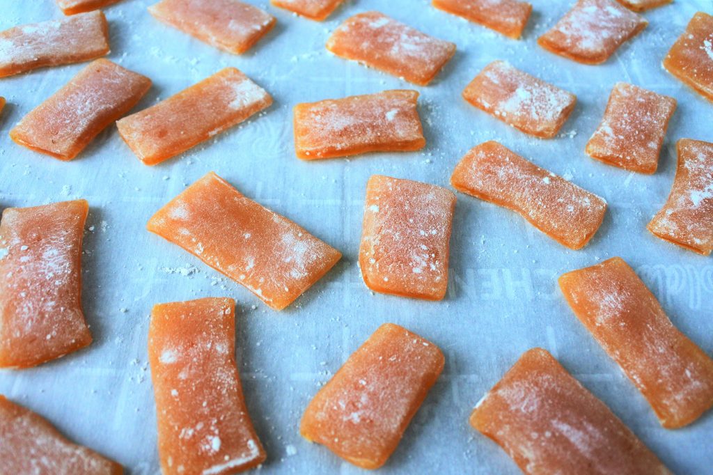 An angled image of flat strips of ginger honey chews dusted with cornstarch on parchment paper