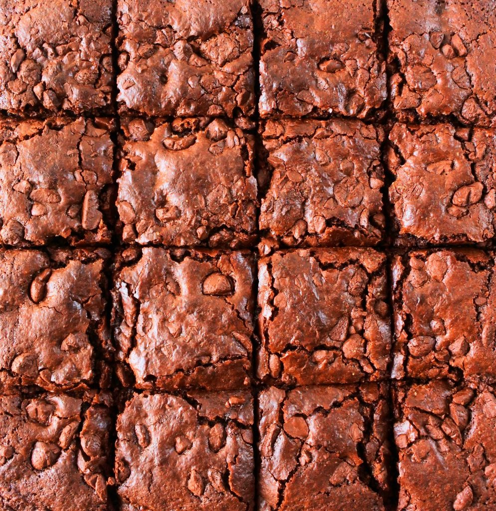 A close up overhead image of a batch of baked chewy gluten free brownies cut into squares