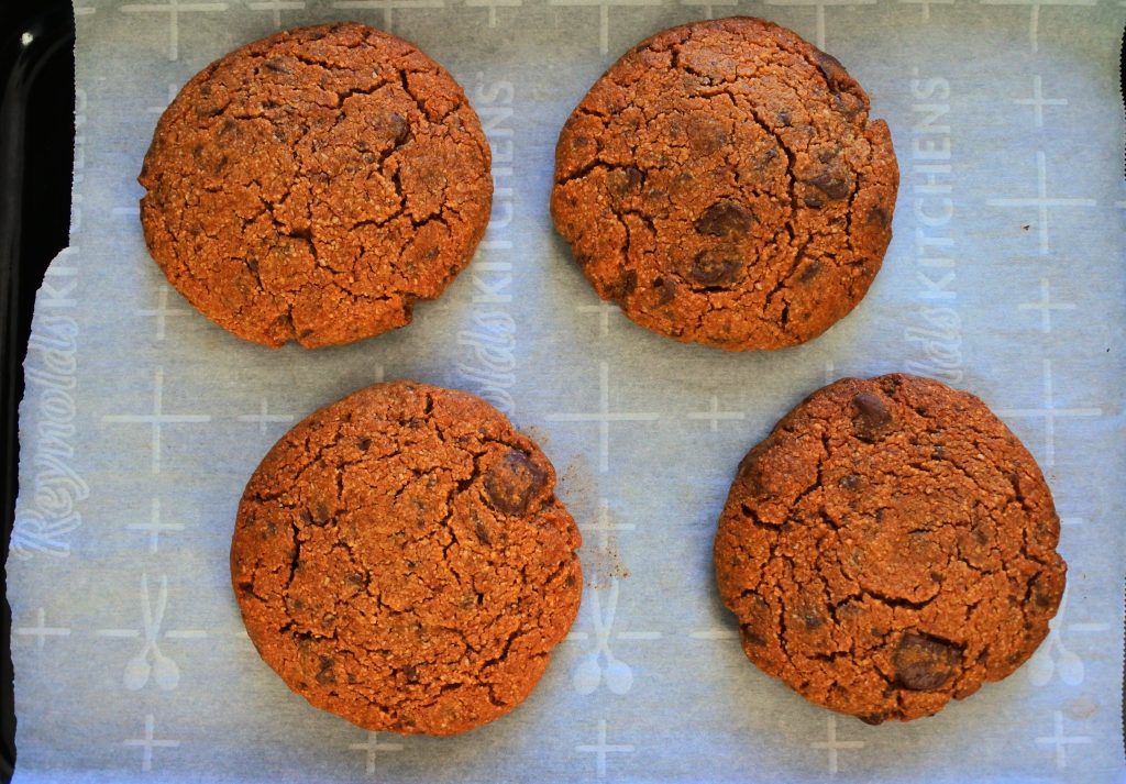 A overhead image of a four baked gluten free chocolate chip cookie on parchment