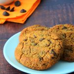 A head on image of a plate of gluten free chocolate chip cookies with a small dish of chocolate chips on an orange cloth napkin in the background