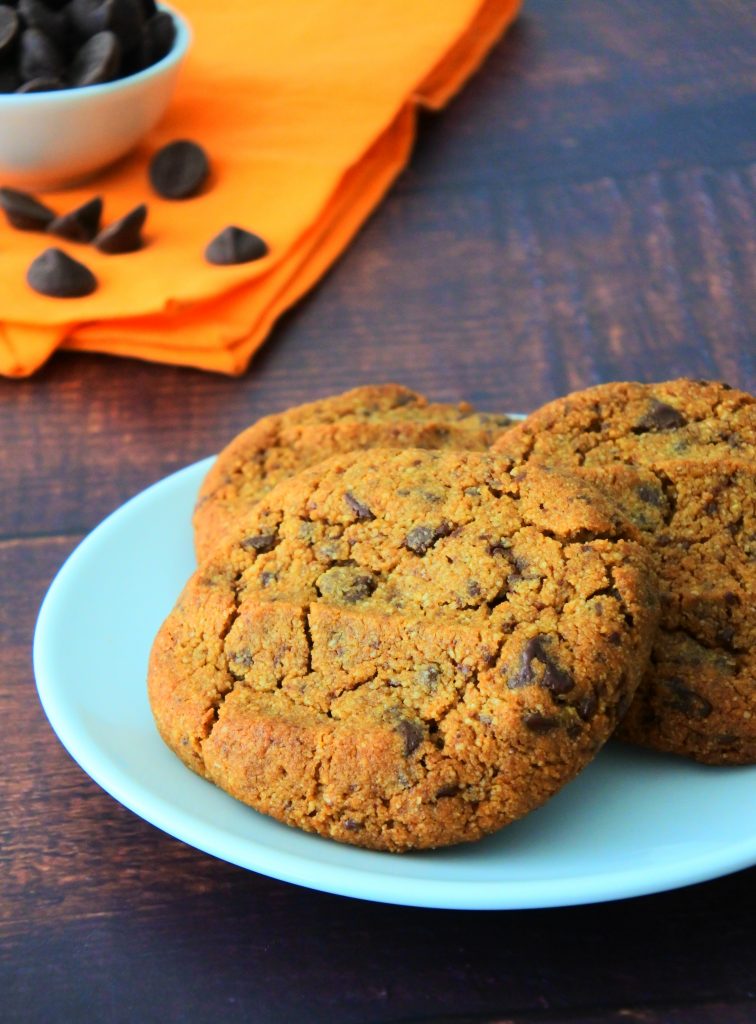 A head on image of a plate of gluten free chocolate chip cookies with a small dish of chocolate chips on an orange cloth napkin in the background