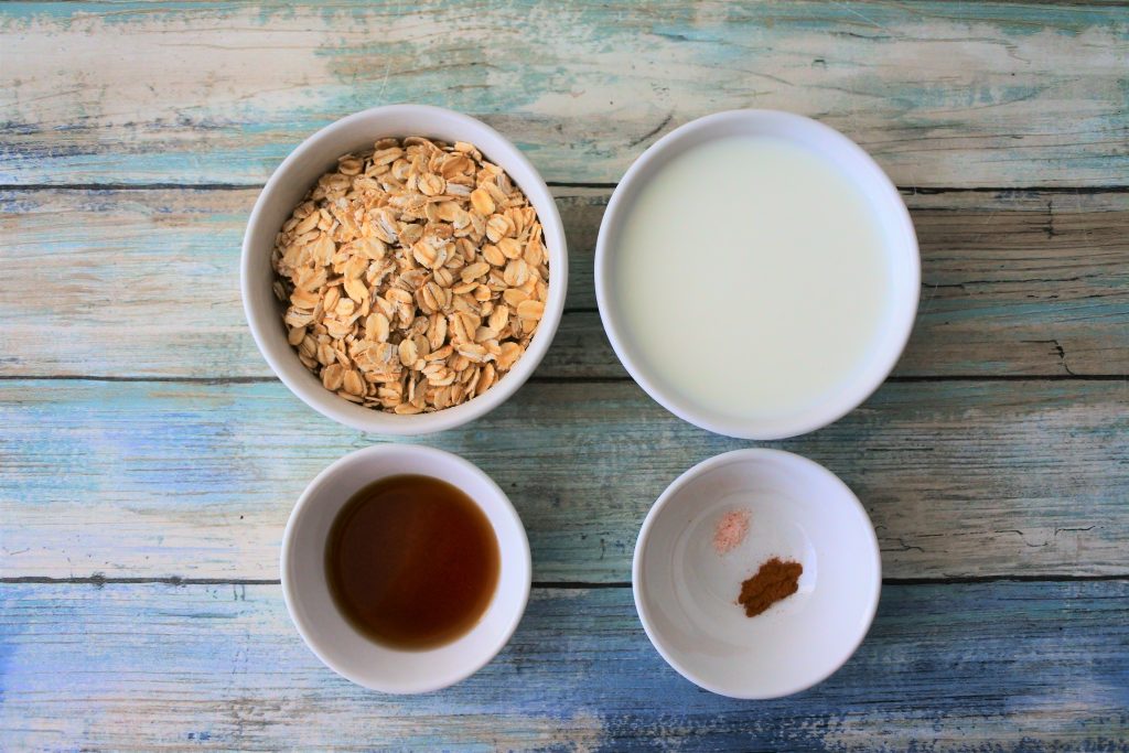 An overhead image of ingredients for overnight oats including oats, milk, maple syrup, salt and cinnamon