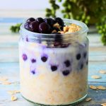 A head on image of a jar of overnight oats topped with wild blueberries