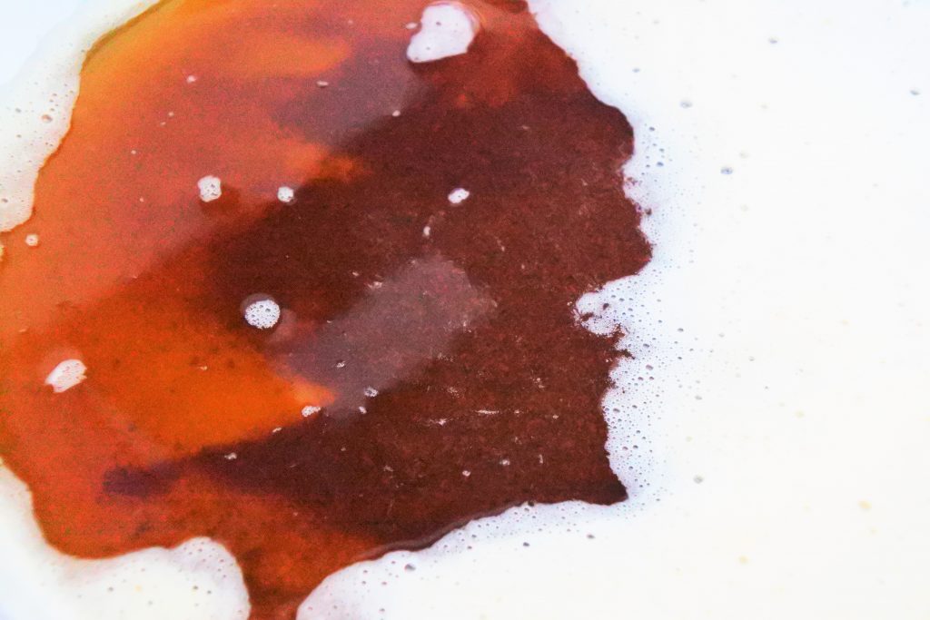 An overhead image of browned butter in a skillet with some of the white foam pushed aside to reveal the browned butterfat and milk solids