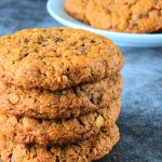 A close up stack of 4 oatmeal chocolate chip cookies with a plate of cookies in the background