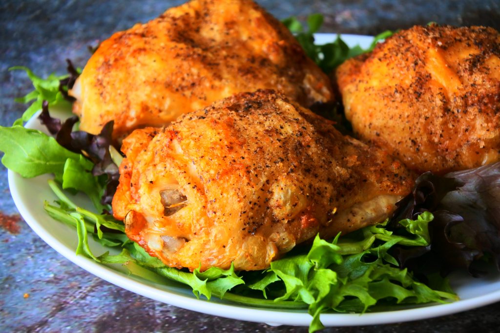 A close up angled image of a white plate of greens with three crispy-skinned air-fried chicken thighs