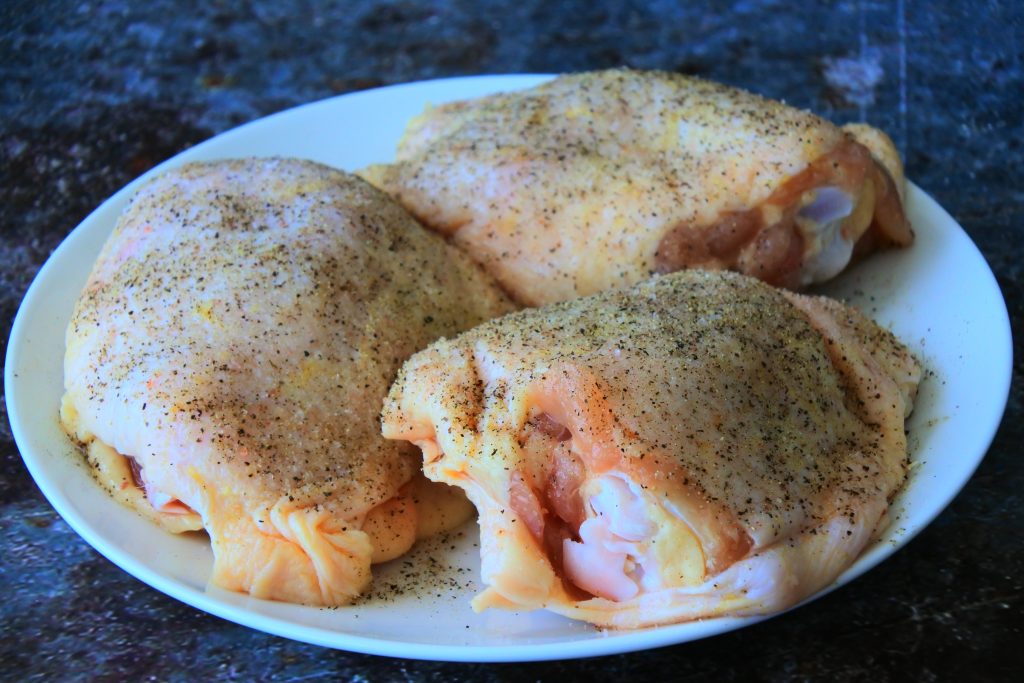 A close up image of raw salt and pepper seasoned chicken thighs on a plate