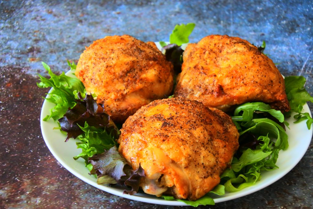 A close up angled image of a white plate of greens with three crispy-skinned air-fried chicken thighs