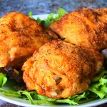 A close up angled image of a white plate of greens with three crispy-skinned air-fried chicken thighs