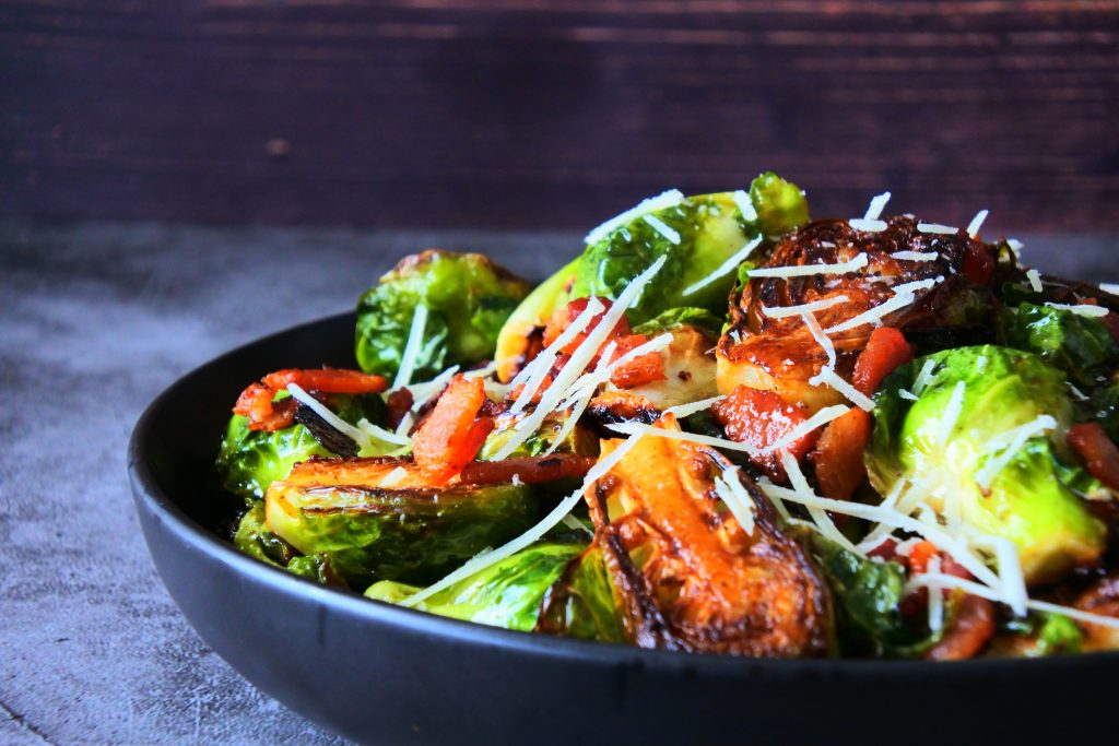 A head on image of a dish of maple bacon brussels sprouts topped with finely shredded cheese