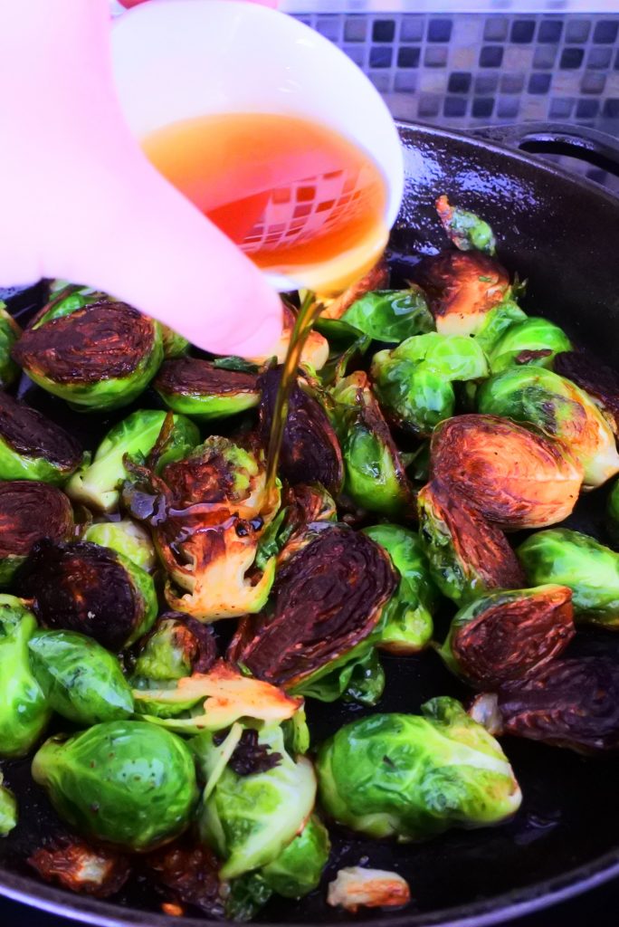 An angled image of a skillet of caramelized brussels sprouts with maple syrup being poured over it.