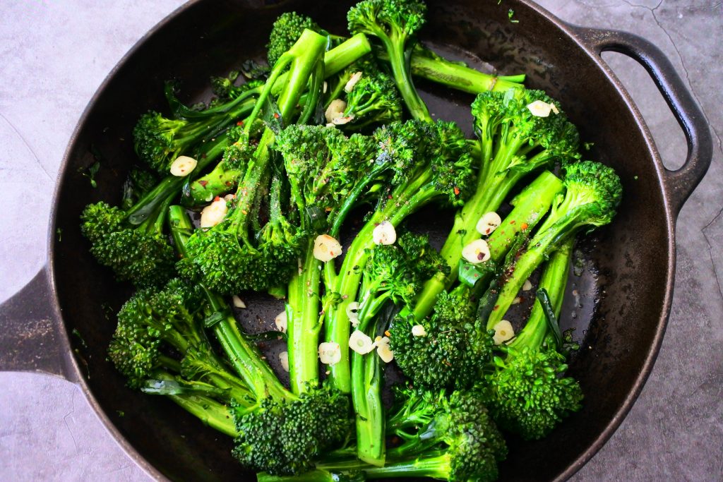 An overhead image of a skillet with sautéed broccolini topped with garlic and seasoning